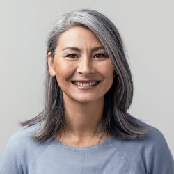 Beautiful asian with grey hair smiling standing near the wall