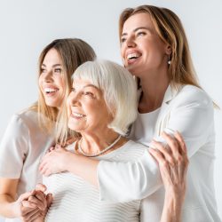 three generation of positive women smiling while hugging isolated on white