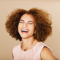 Fashion studio portrait of stylish middle age woman posing on beige background, laughing 50 - 55 year old lady with curly hair